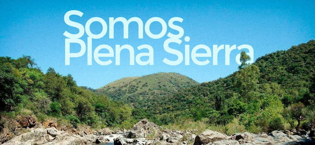 paisaje de las sierras de córdoba, con río, montañas y una abundante vegetación, sobre el cielo celeste se visualiza la frase Somos Plena Sierra